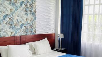 Habitación de hotel con una cama grande, una mesita de noche, una lámpara y una ventana con cortinas.