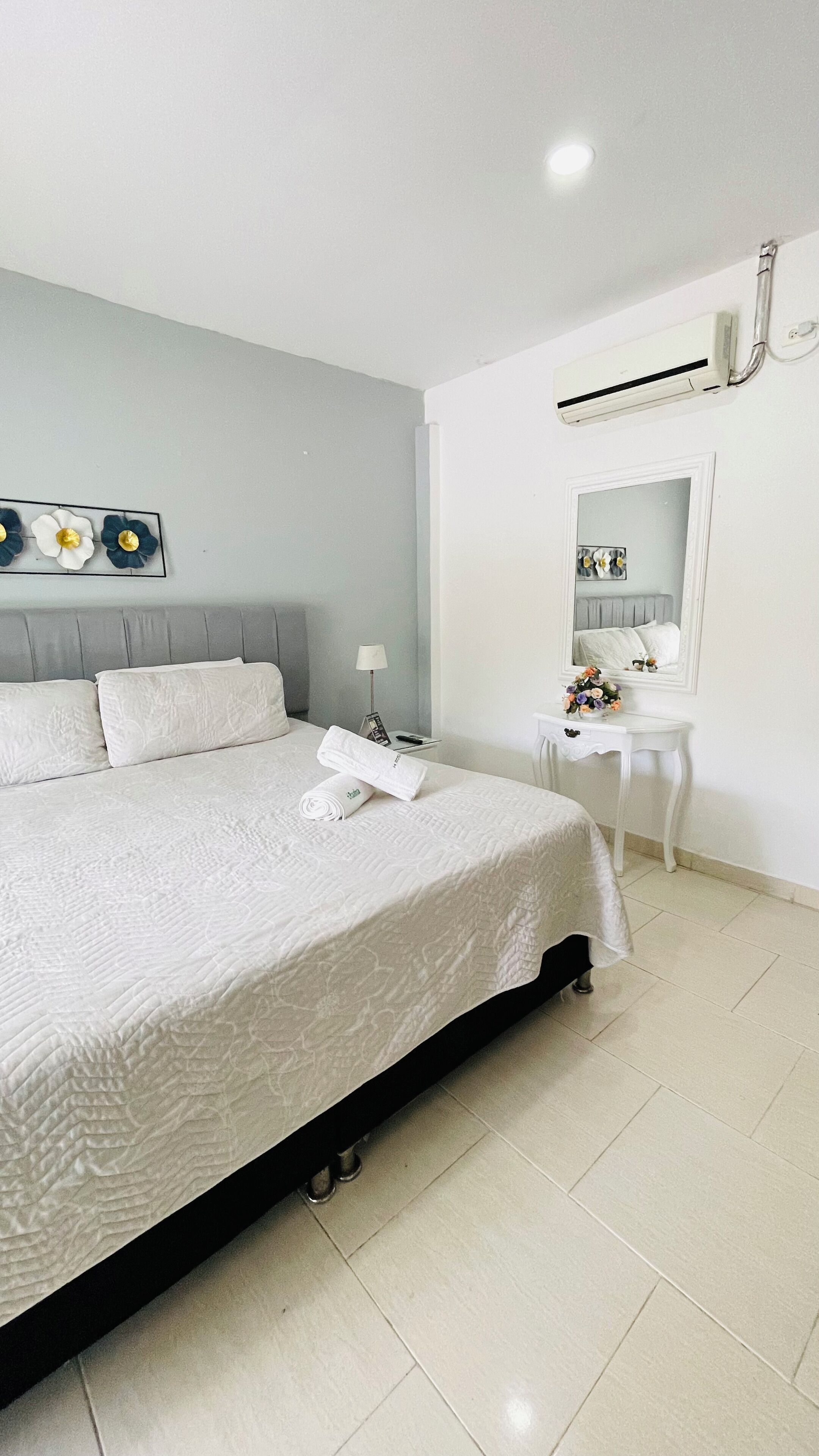 Una habitación de hotel con cama, mesita de noche con lámpara, espejo y aire acondicionado.