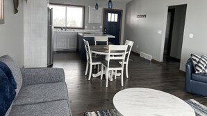 A modern kitchen with white cabinets, a dining area with a white table and chairs, and a living room with a gray sofa and a blue couch.