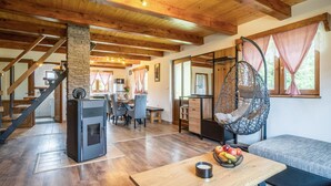 Una sala de estar acogedora con chimenea de piedra, vigas de madera, un sillón colgante y un comedor con mesa y sillas.