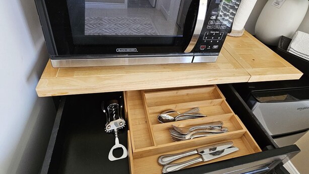 A kitchen with a microwave, a wooden cutting board, and a drawer with utensils.