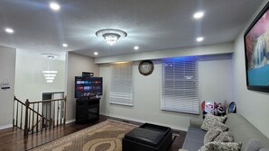 A living room with a flat-screen TV, a clock, and a painting on the wall. - Niagara Luxury villa-Breakfast, pool, water view (Niagara Falls)