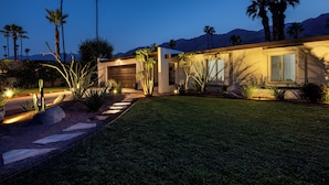 Una casa moderna con césped cuidado, palmeras y un garaje.
