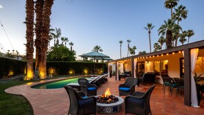 Un patio con una fogata, asientos al aire libre y una piscina.