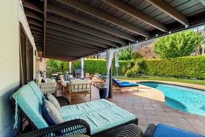 An outdoor patio with a pool, lounge chairs, and a covered seating area.