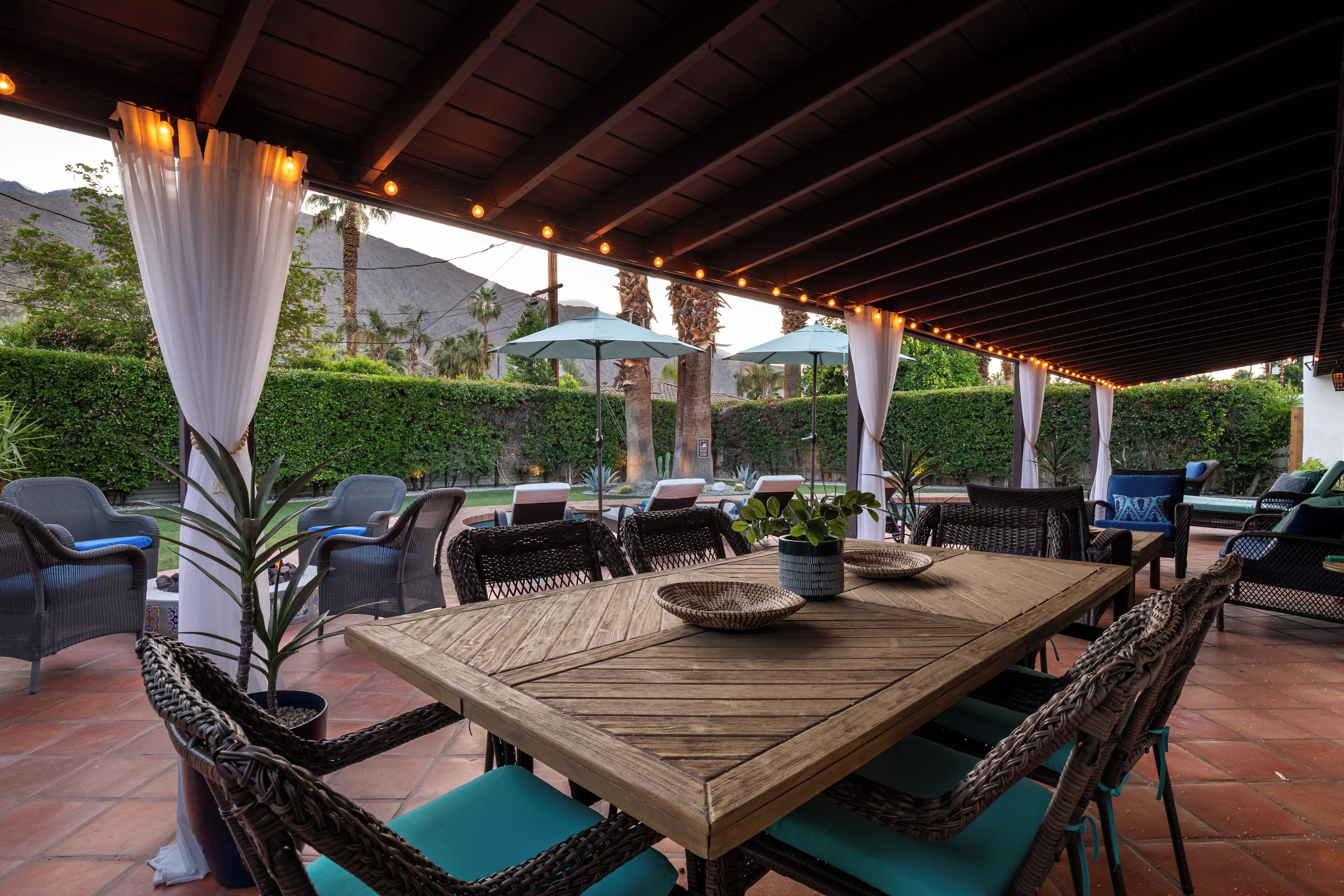 Un patio al aire libre con una mesa de madera, sillas de mimbre y sombrillas.