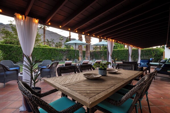 An outdoor patio with a wooden table, wicker chairs, and umbrellas.