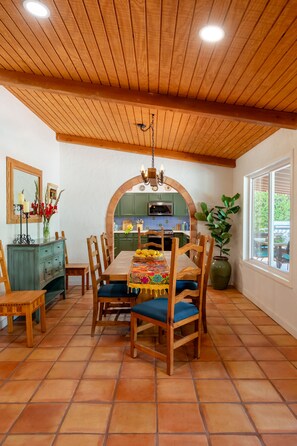 A dining area with a wooden ceiling, tiled floor, and a view of the kitchen through an arched doorway. - Casa Fierro: 3-bed Superior Spanish retreat in south Palm Springs (Palm Springs)