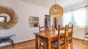 A dining area with a wooden table and chairs, a woven pendant light, a mirror, and a shelf with books and decorative items. - Beautiful home in Periana (Periana)