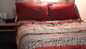 Una cama con ropa de cama estampada, una mesita de noche con un reloj y dos cuadros en la pared.