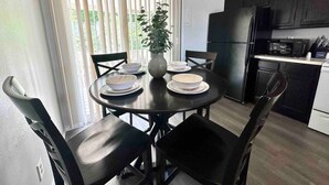 A modern kitchen with black cabinets, a black refrigerator, and a microwave. There is a dining table with four chairs and a vase with a plant. - The Hygge Apt B (Colorado Springs)