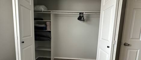A walk-in closet with white doors, shelves, and a hanging rod.