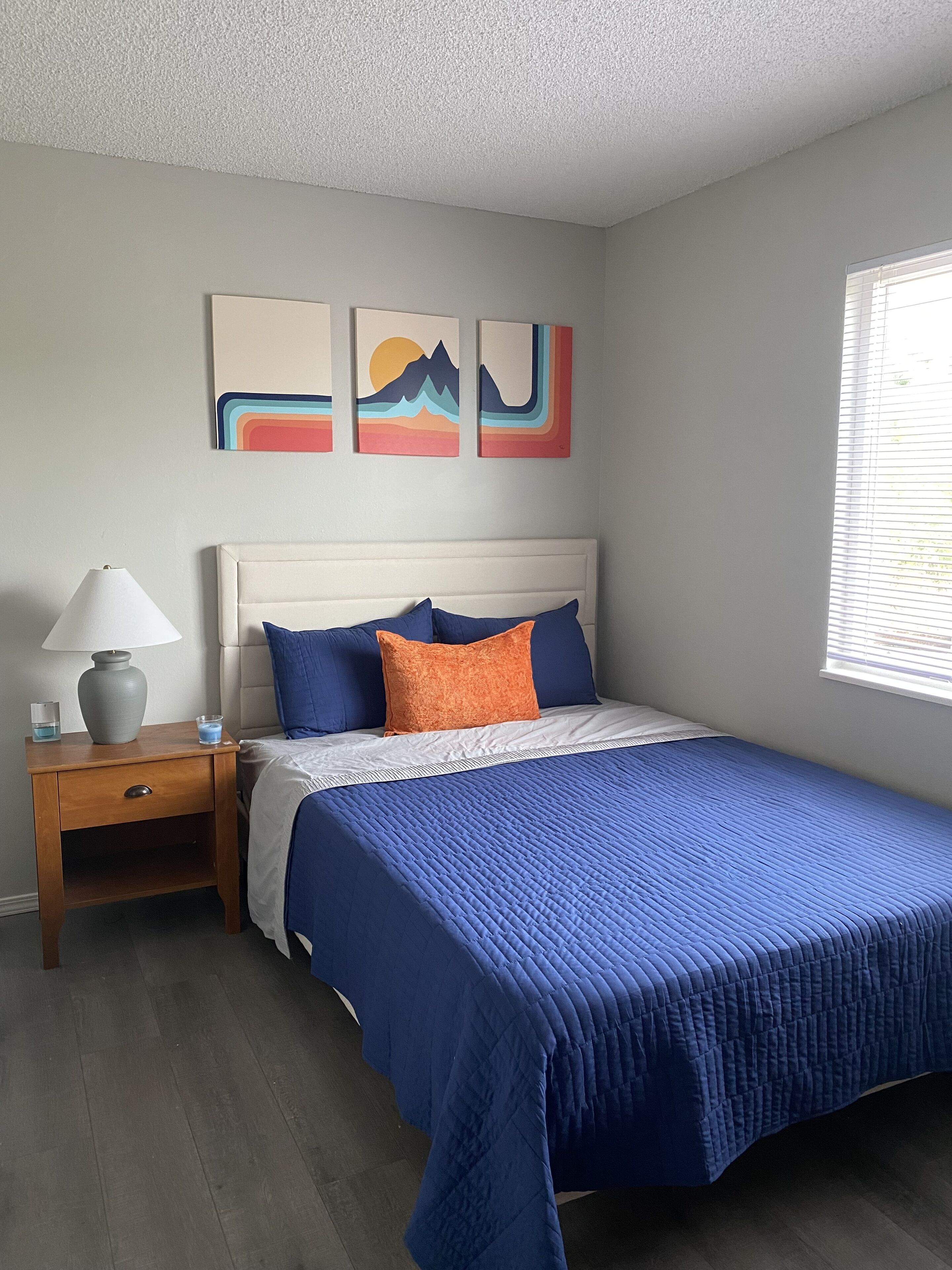 A bedroom with a bed, a nightstand, a lamp, and wall art.