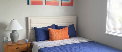 A bedroom with a bed, a nightstand, a lamp, and wall art.