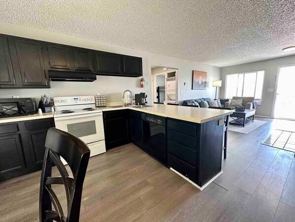 Una cocina moderna con armarios oscuros, una isla central y un área de comedor con sofá y mesa de centro.