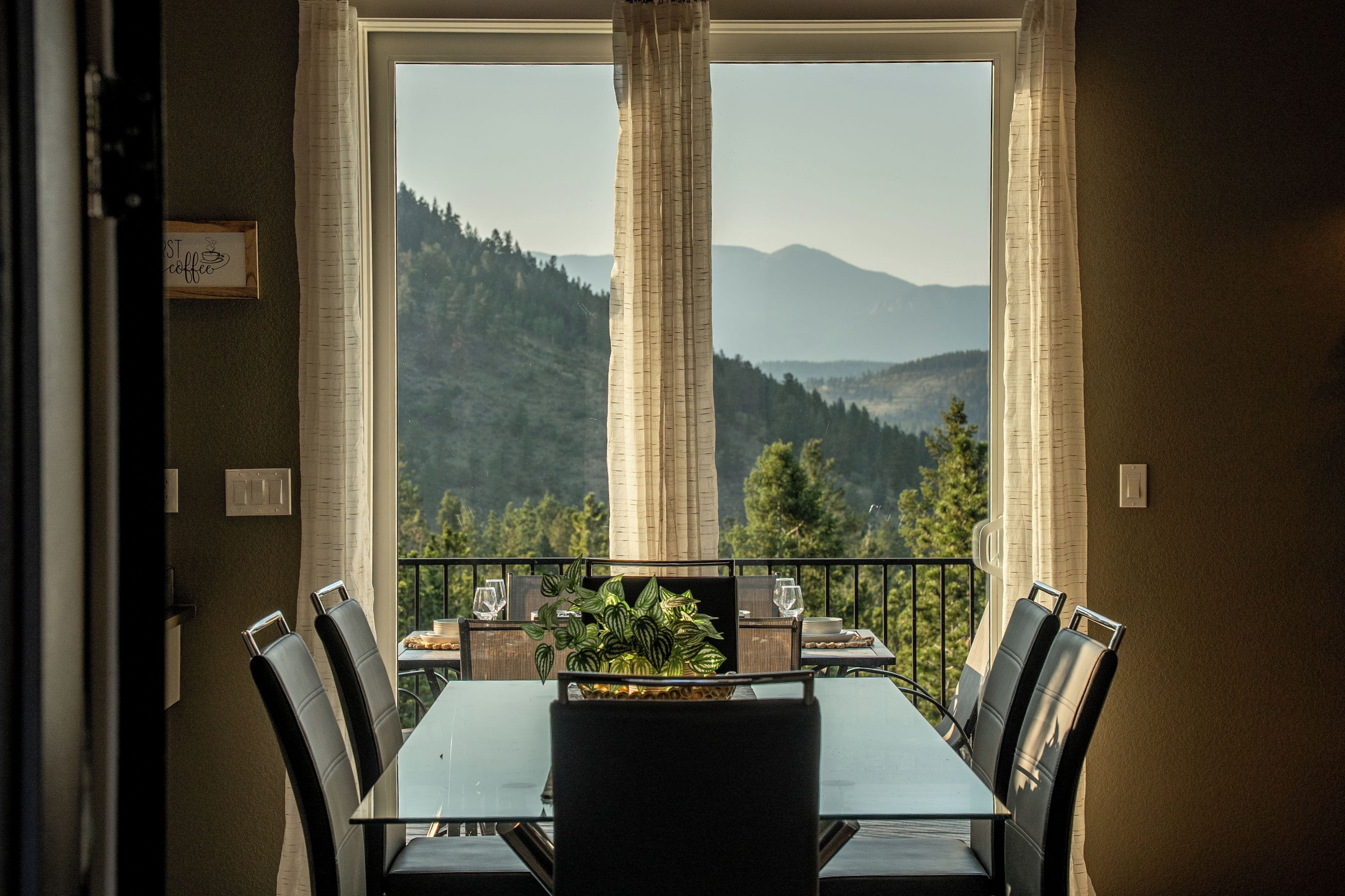 A dining area with a table and chairs, a view of mountains, and a balcony with a railing.