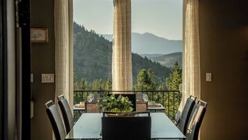 A dining area with a table and chairs, a view of mountains, and a balcony with a railing.