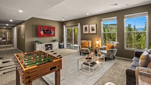 A living room with a foosball table, a fireplace, and large windows offering a view of the outdoors.