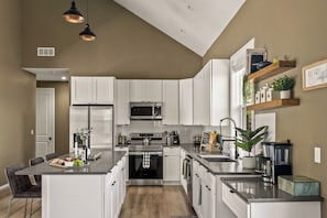 Una cocina moderna con muebles blancos, electrodomésticos de acero inoxidable y una isla central.
