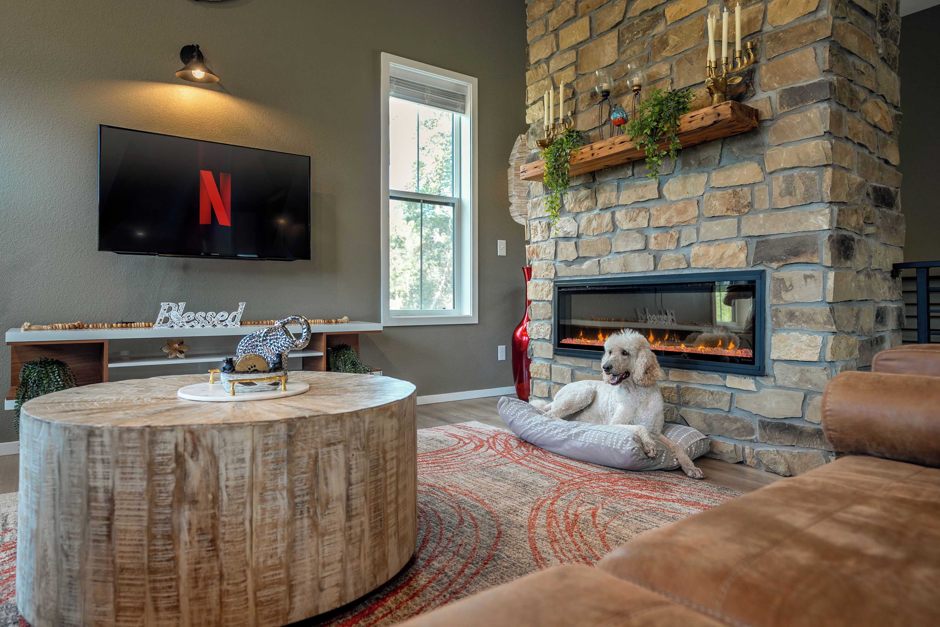 Una sala de estar acogedora con chimenea de piedra, un televisor de pantalla plana y un perro descansando sobre un cojín.