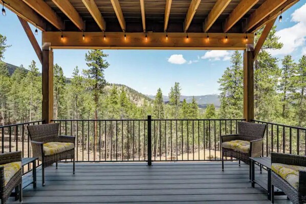 A covered outdoor deck with wicker furniture and a view of a forested mountain range.