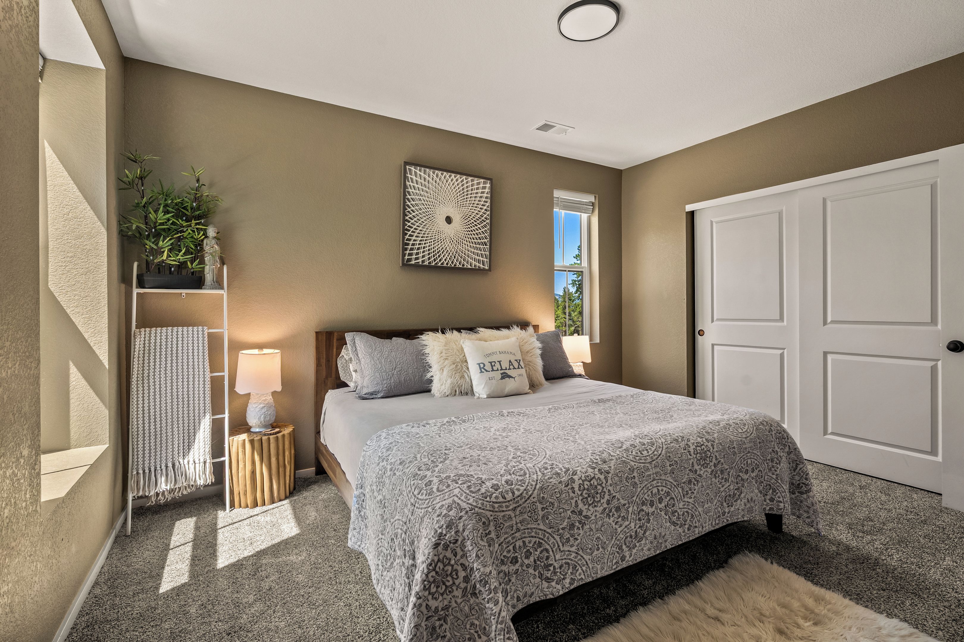 Un dormitorio con cama, mesita de noche, lámpara de pared, un adorno en la pared, una ventana y una puerta.