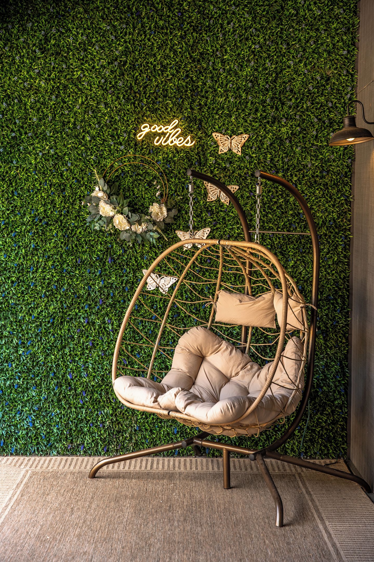 A hanging chair with a cushion and a neon sign saying 'good vibes' against a green leafy wall.