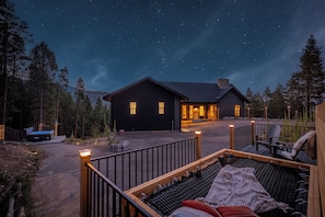Una cabaña con terraza, rodeada de árboles, bajo un cielo estrellado.