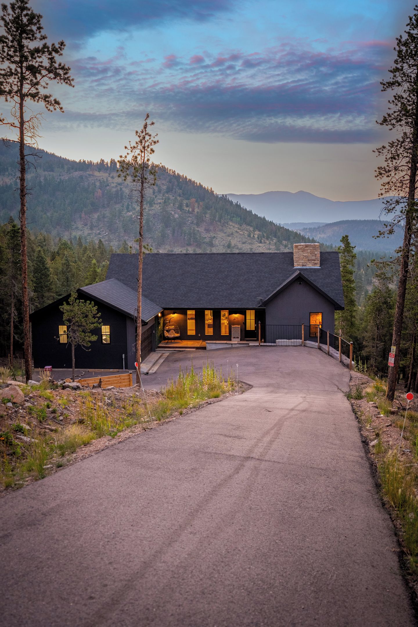 A modern building with a dark exterior, a paved driveway leading to the entrance, and a view of a forested mountain range in the background.