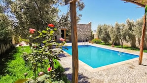 Una piscina con un edificio in pietra sullo sfondo, circondata da vegetazione e alberi.