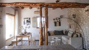 Un soggiorno rustico con travi a vista in legno, un muro in pietra, un divano e una zona pranzo con tavolo e sedie.
