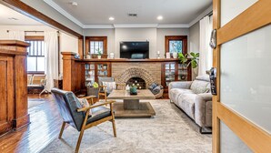 A spacious living room with a fireplace, wooden furniture, and a flat-screen TV mounted on the wall.