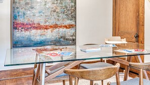 Una habitación moderna con una mesa de vidrio, sillas de madera, un cuadro abstracto grande y una puerta de madera.