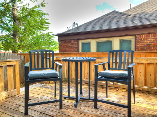 Una terraza de madera con dos sillas de metal negro y una pequeña mesa redonda.