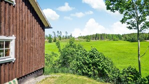 Een houten gebouw met een raam, omringd door een groen veld en bomen.