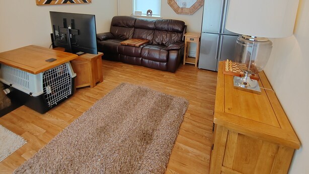 A compact living space with a sofa, a TV, a wooden table, a fridge, and a rug. - Castle Cottage View (Harlech)