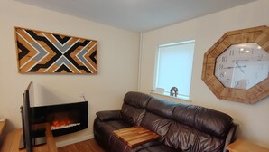 A living room with a leather sofa, a fireplace, a wooden coffee table, a wall clock, and a geometric art piece. - Castle Cottage View (Harlech)