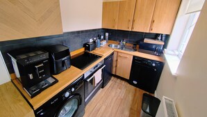 A compact kitchen with a washing machine, dishwasher, and a coffee maker. - Castle Cottage View (Harlech)
