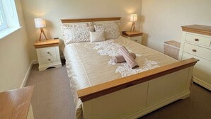 A bedroom with a large bed, two bedside tables, a hanging light fixture, and a window. - Castle Cottage View (Harlech)
