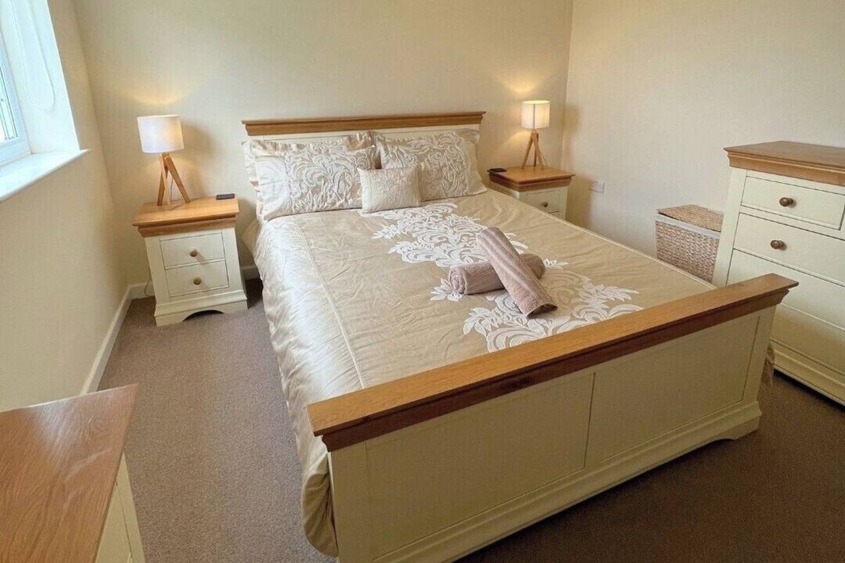 A bedroom with a large bed, two bedside tables, a hanging light fixture, and a window.