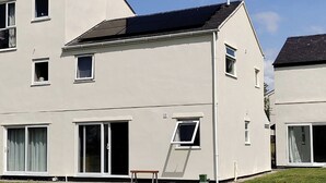 A modern two-story residential building with a flat roof, large windows, and a sliding glass door. - Castle Cottage View (Harlech)