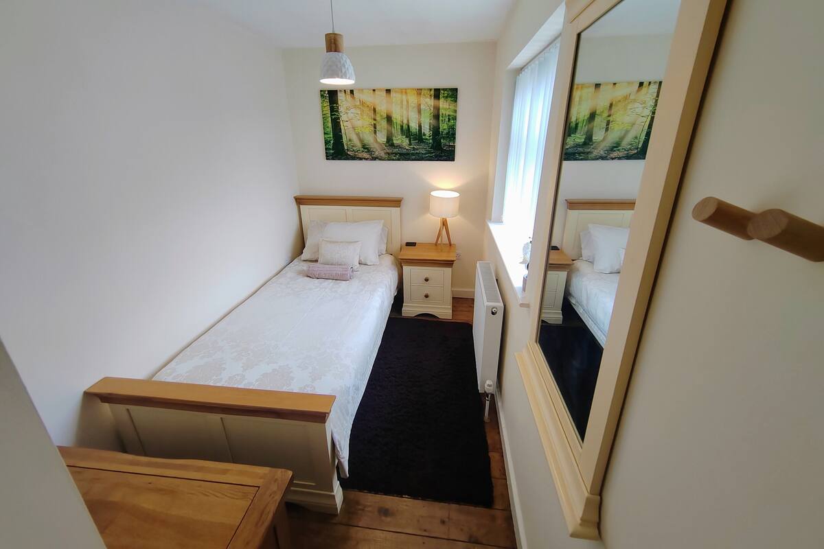 A bedroom with a single bed, a bedside table with a lamp, a radiator, and a large mirror.