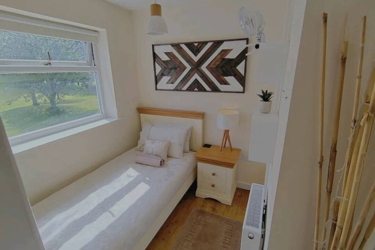 A bedroom with a bed, bedside table, lamp, and a decorative wall piece.