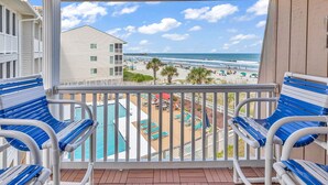 A balcony with two blue and white striped chairs, a pool, and a view of the beach and ocean.