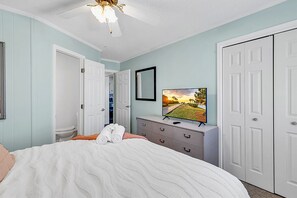A bedroom with a bed, a television on a dresser, and a door leading to a bathroom.