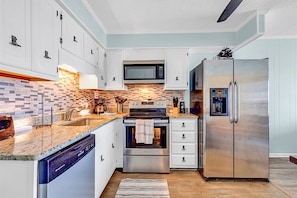 A modern kitchen with white cabinets, a stainless steel refrigerator, an oven, and a microwave.