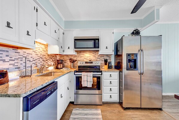 Una cocina moderna con armarios blancos, un refrigerador de acero inoxidable, un horno y un microondas.