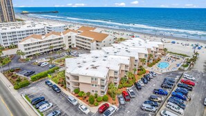 A hotel with multiple buildings, a parking lot, and a beach view.