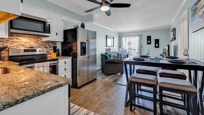 A modern kitchen with stainless steel appliances, a dining area with a bar, and a ceiling fan.