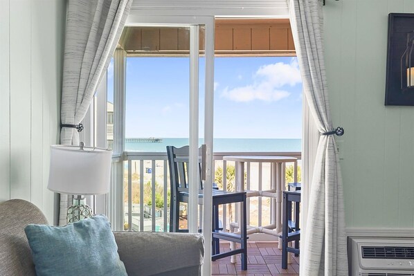 A room with a view of the sea, a balcony with chairs, and a table.